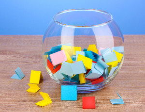 Pieces of paper for lottery in vase on wooden table on blue background