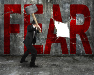 businessman holding sledgehammer hitting red FEAR word on concrete wall